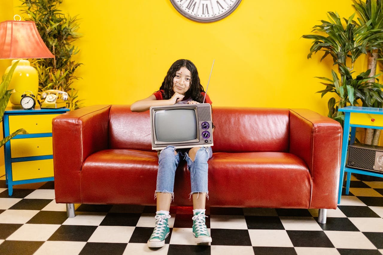 team-04 A young woman with a CRT TV sits on a red couch in a colorful living room.