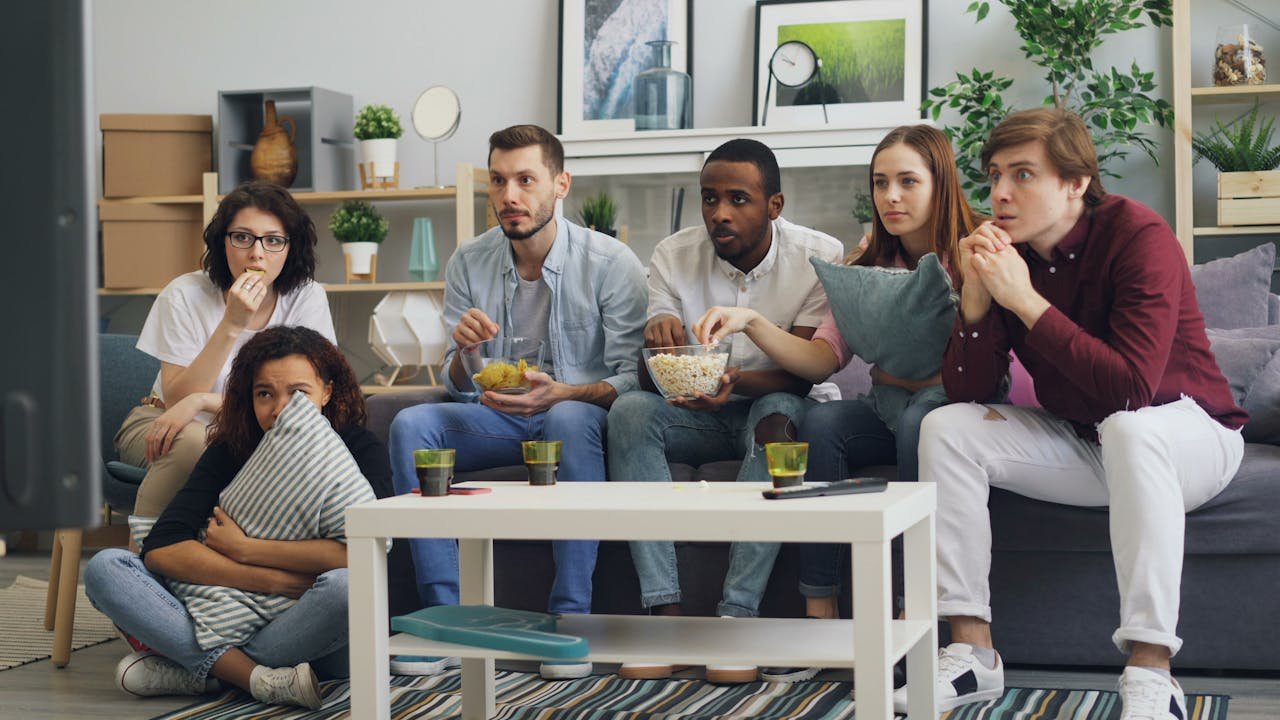 Group of friends watching a movie on a couch, enjoying snacks and drinks indoors.